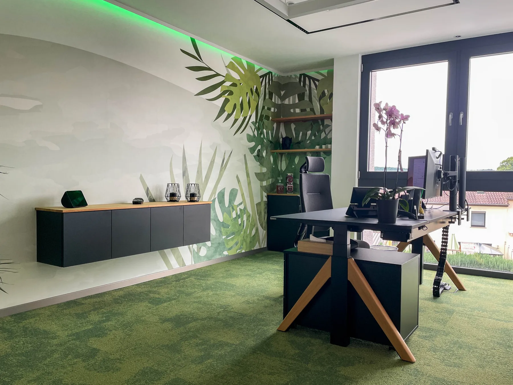 Büro mit grünem Boden, Pflanzen-Wandbild und grüner Lichtleiste im Firmensitz von Merios