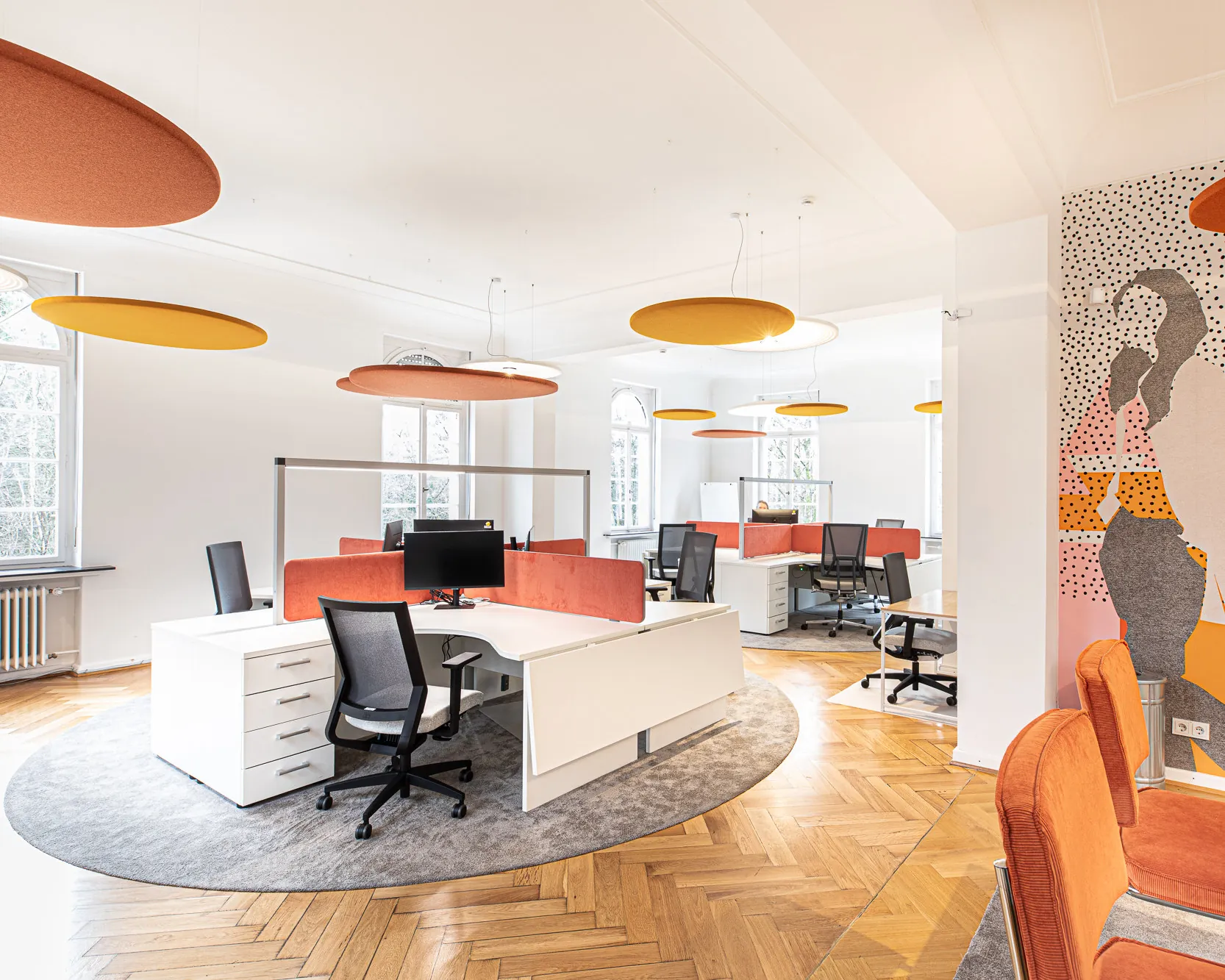 Großraumbüro für die Mitarbeitenden mit weißen Tischen und orangefarbenen Deckensegeln in der Villa von m&r Kreativ