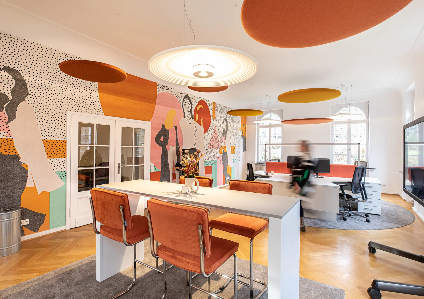 Büro mit Meetingbereich, orangefarbenen Stühlen, farbigem Wandbild und runden Deckensegeln in der Villa von m&r Kreativ